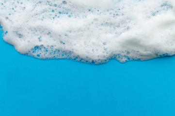 The soapy foam texture flows down from the top on a blue background. The concept of hygiene.