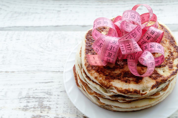 a stack of pancakes on a plate with a centimeter tape on top on a wooden table. the concept of an...