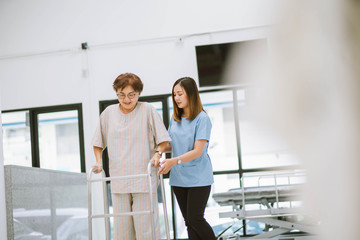 young physical therapist helping senior patient in using walker during rehabilitation - obrazy, fototapety, plakaty