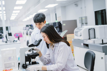 Two  medical  scientist working in Medical laboratory , young female scientist looking at microscope and young male look at report on his hand