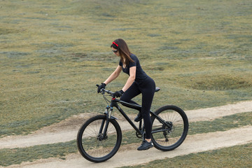 Girl on a mountain bike on offroad, beautiful portrait of a cyclist in rainy weather, Fitness girl rides a modern carbon fiber mountain bike in sportswear. Close-up portrait of a girl in red bandana.