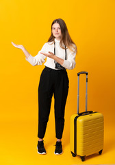 Full body of traveler teenager girl with suitcase over isolated yellow background extending hands to the side for inviting to come