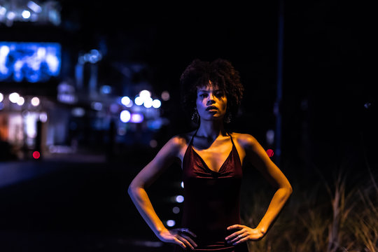 Stylish african american woman in night city. Woman standing with hands on waist. Background with blurred yellow and blue light. Half-length portrait