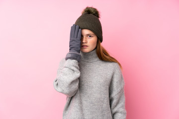 Ukrainian teenager girl with winter hat over isolated pink background covering a eye by hand