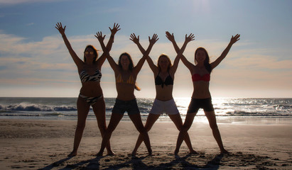 Silhouette of four beautiful women standing with their hadnss in the air on a beach at sunset or sunrise.