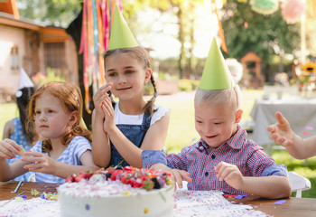 Down syndrome child with friends on birthday party outdoors in garden.