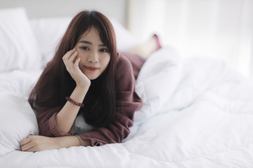 Portrait of beautiful young Asian woman is lying in bed with white curtain background.