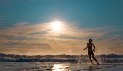 Silhouette of two beautiful women running on a beach shore with waves in the background at sunset or sunrise.