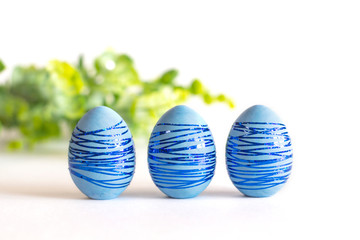 Three blue Easter eggs with blue shiny stripes on a white background.