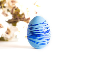 Blue Easter egg with blue shiny stripes on a white background. With a green branch in the background.