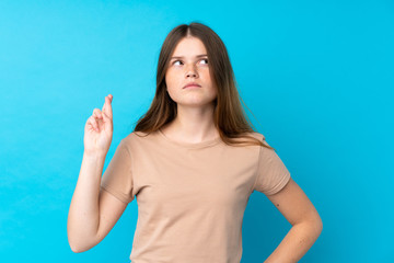 Fototapeta premium Ukrainian teenager girl over isolated blue background with fingers crossing and wishing the best