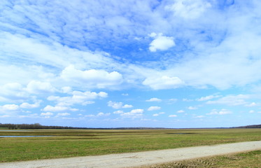 Farm road, green meadow and blue sky in background