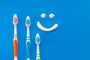 Multicolored toothbrushes on a blue background with a smile painted with toothpaste. The view from the top.