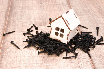 a wooden small house with a window stands on a pile of black screws, a house on nails, wooden...