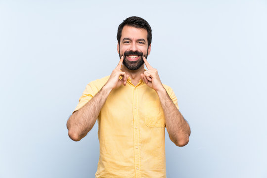 Young man with beard over isolated blue background smiling with a happy and pleasant expression