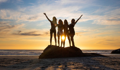 Silhouette of four beautiful women standing on a rock on a beach at sunset or sunrise.