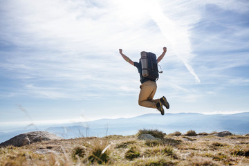 Rear view of man with backpack hiking in mountains in summer, jumping.