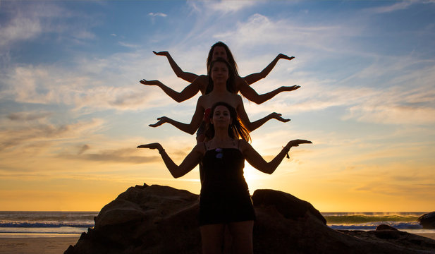 Silhouette of four beautiful women creating a Hindu Godess shape on a rock on a beach at sunset or sunrise.