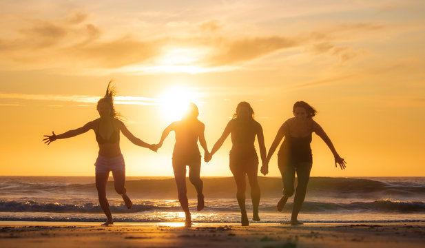 Silhouette of four beautiful women having fun running and jumping on a beach at sunset or sunrise.