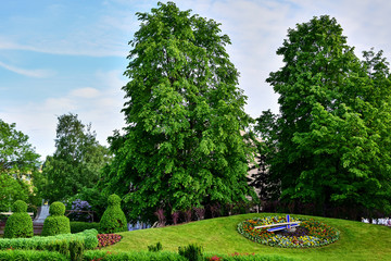 Ventspils, Latvia - Flower bed in the form of flowers on a hill with green grass, nearby bushes in the form of figures and trees, a street in the summer afternoon.