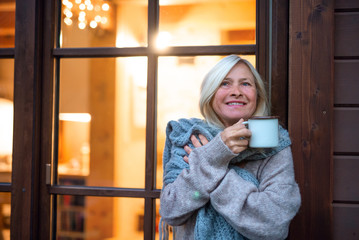 Senior woman with coffee standing outdoors on terrace, resting.