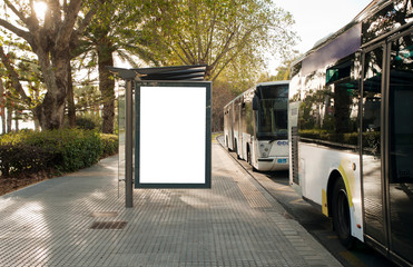 White blank vertical billboard at the bus stop, with two buses on the city street. In the background of buses and roads. Sketch. Poster on the street next to the road.