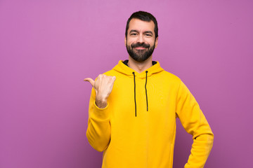 Handsome man with yellow sweatshirt pointing to the side to present a product