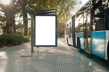 White blank vertical billboard at the bus stop on the city street. In the background of buses and...