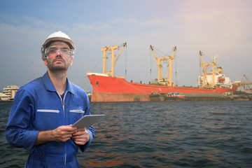 Caucasian man engineer staff worker with tablet in hand and tanker container ship background...