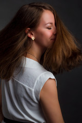 A photo of a woman with brown straight hair posing in white shirt on dark background in Studio. hair dynamic motion