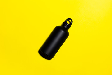 Close-up of black reusable aluminum thermo bottle for water on yellow background.