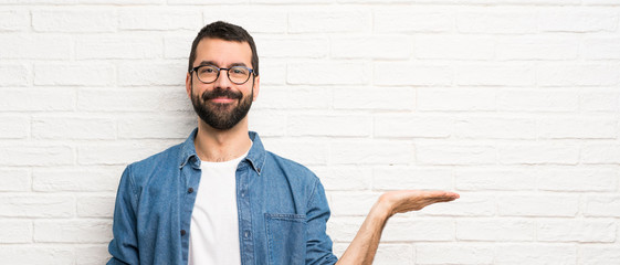 Handsome man with beard over white brick wall holding copyspace imaginary on the palm to insert an ad