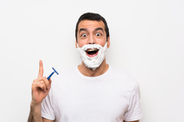 Man shaving his beard over isolated white background thinking an idea pointing the finger up