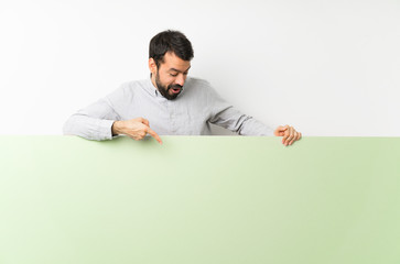 Young handsome man with beard holding a big green empty placard and pointing it