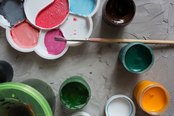 Gouache for drawing different colors with brushes on a gray texture background. Gouache cans are randomly located. Background gray textural brush strokes