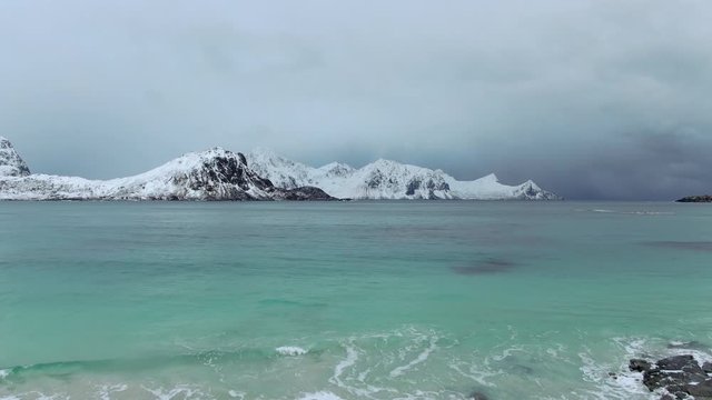 snow covered haukland beach  lofoten aerial view drone fly low on seashore and rises up over water norway