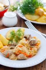 Sauerkraut stew with meat on a white plate with potatoes, selective focus