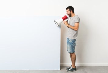 Young handsome man with beard holding a big blue empty placard shouting through a megaphone