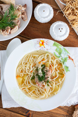 Homemade noodles with chicken in a white plate on a wooden table, selective focus