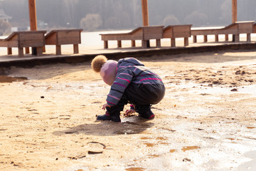 child 3-4 years old in a hat and overalls poking around in the mud near a large dirty pool