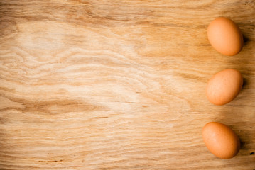Three brown eggs lie on a wooden surface