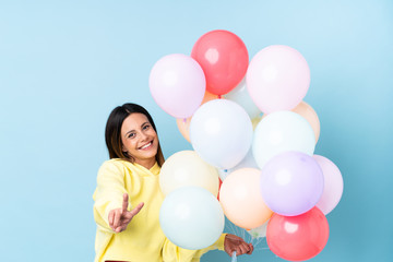 Fototapeta na wymiar Woman holding balloons in a party over isolated blue background smiling and showing victory sign