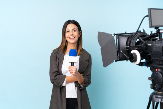 Reporter woman holding a microphone and reporting news over isolated blue background laughing