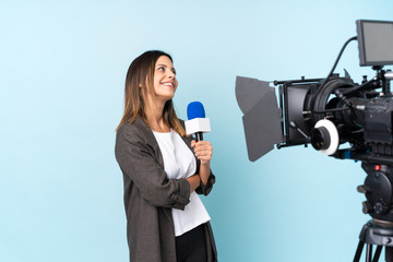 Reporter woman holding a microphone and reporting news over isolated blue background laughing