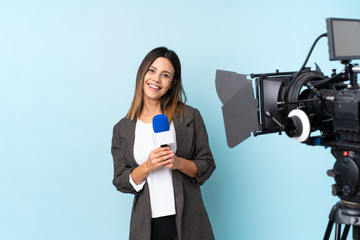 Reporter woman holding a microphone and reporting news over isolated blue background applauding