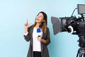 Reporter woman holding a microphone and reporting news over isolated blue background pointing with the index finger a great idea