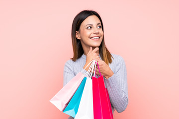 Woman over isolated pink background holding shopping bags and thinking