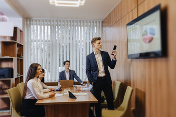 Meeting of office workers at the table, looking at the presentation with diagrams on the TV