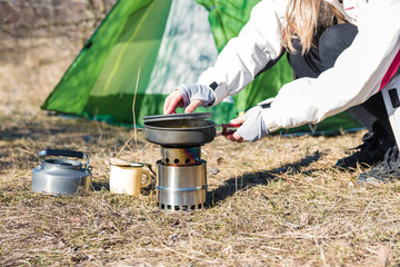 camping and cooking. woman hiker cooking lunch in front of her tent in nature