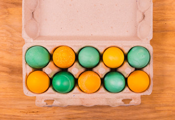 Yellow and green eggs in a carton on a wooden background